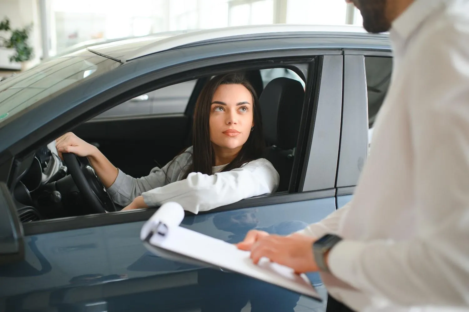 A driver at the wheel going over paperwork with an agent standing at the car window